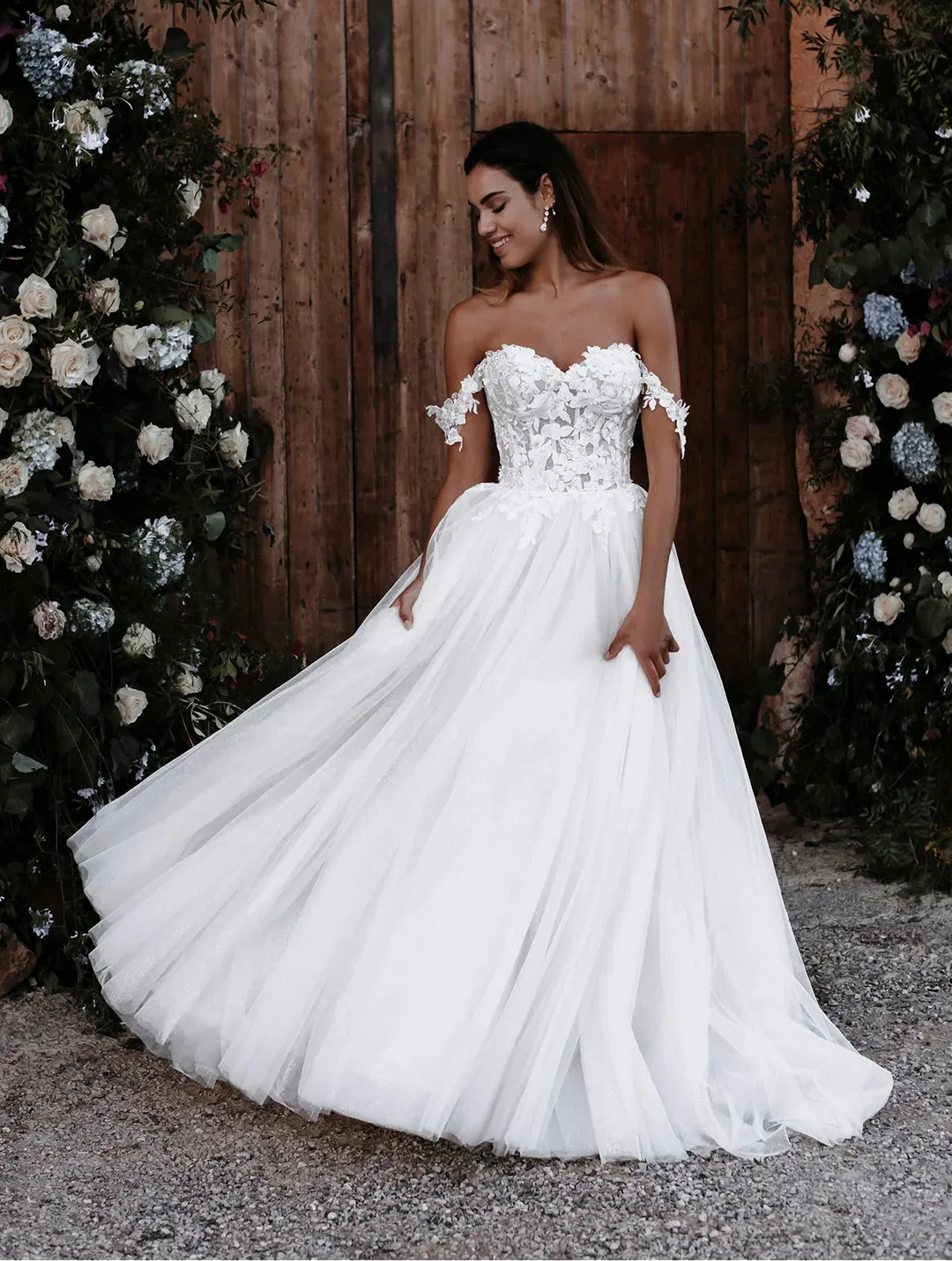Woman in a white wedding dress standing in front of a wooden door with floral decorations.