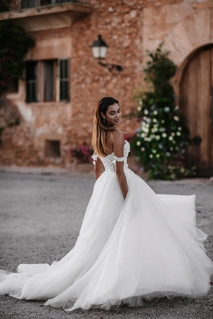 Woman in a white wedding dress standing in front of a stone building with greenery.
