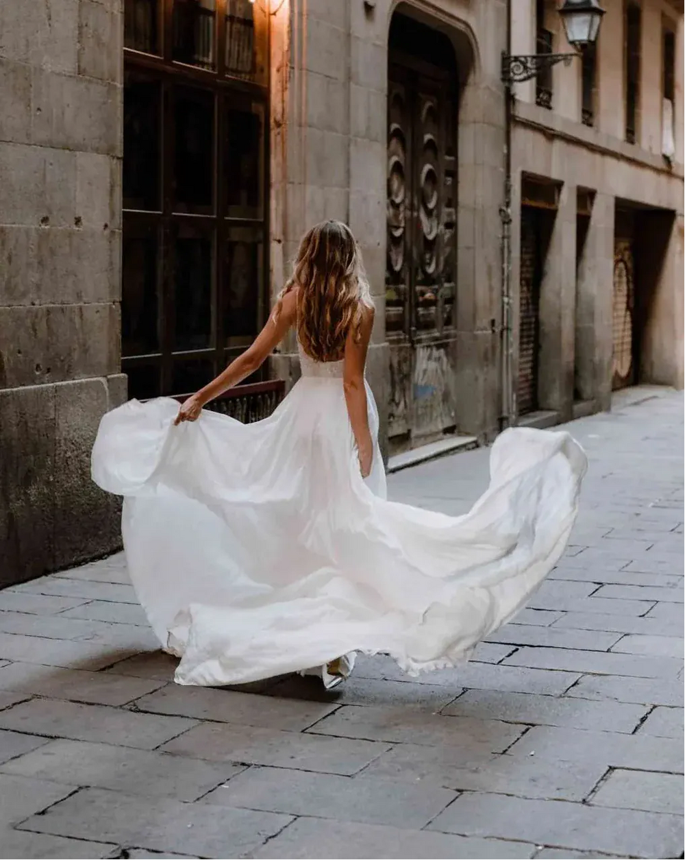 Woman in a white dress walking down a cobbled street with stone buildings.