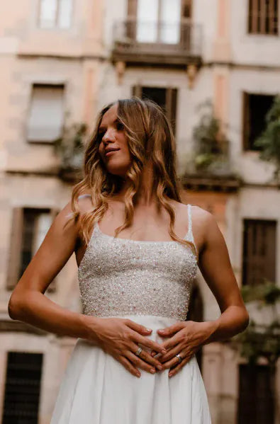 Woman in a silver sequin top and white skirt standing in an urban setting.
