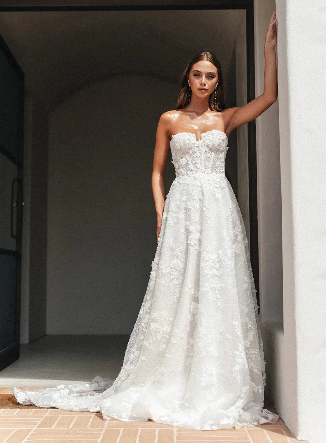 Woman in a strapless white wedding dress standing in a sunlit room.