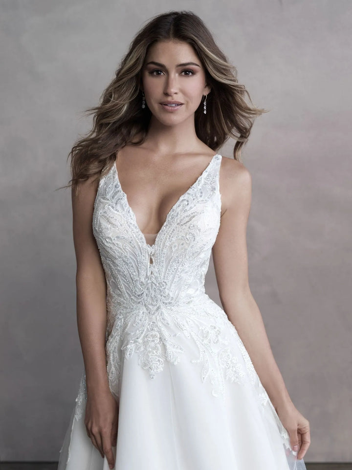 A woman modeling a white sleeveless wedding dress with a deep V-neckline, lace bodice, and flowing skirt against a textured gray studio backdrop.