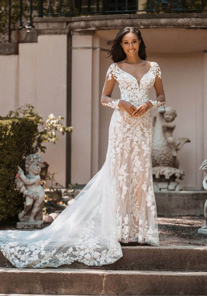Woman in a lace wedding dress standing on steps with classical sculptures in the background