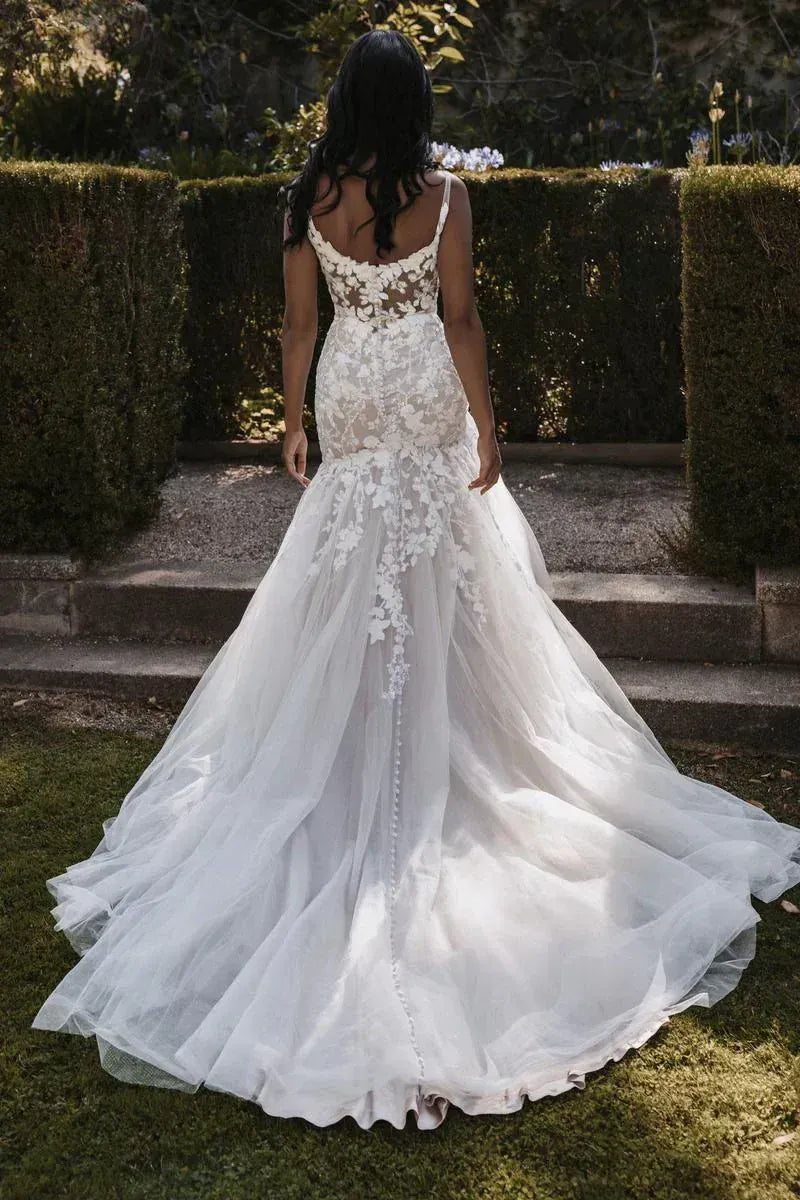 Woman wearing a white wedding dress with floral details in an outdoor setting.
