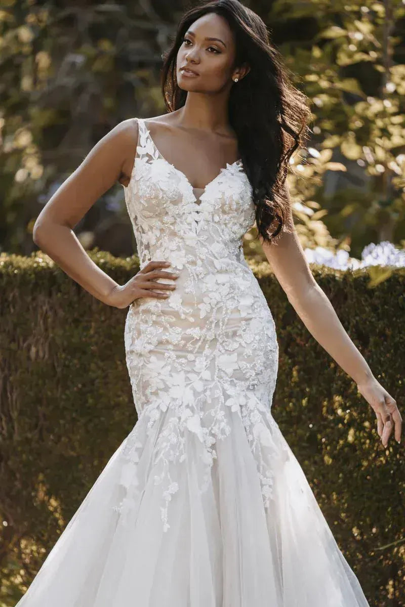Woman wearing a white lace wedding dress outdoors with greenery in the background
