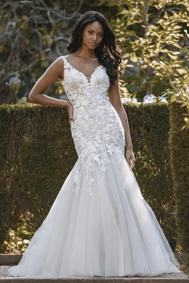 Woman wearing a white wedding dress with floral details against a natural background