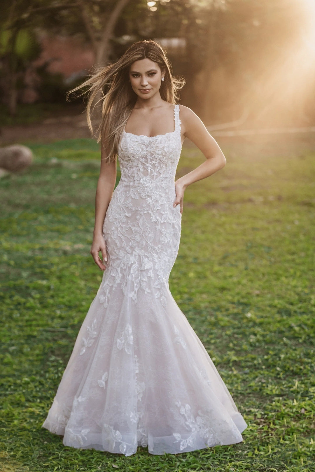 Woman in a white lace wedding dress standing in a grassy field with a blurred background