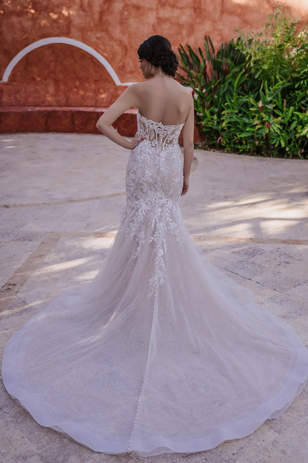 Woman in a white wedding dress with intricate detailing standing outdoors.