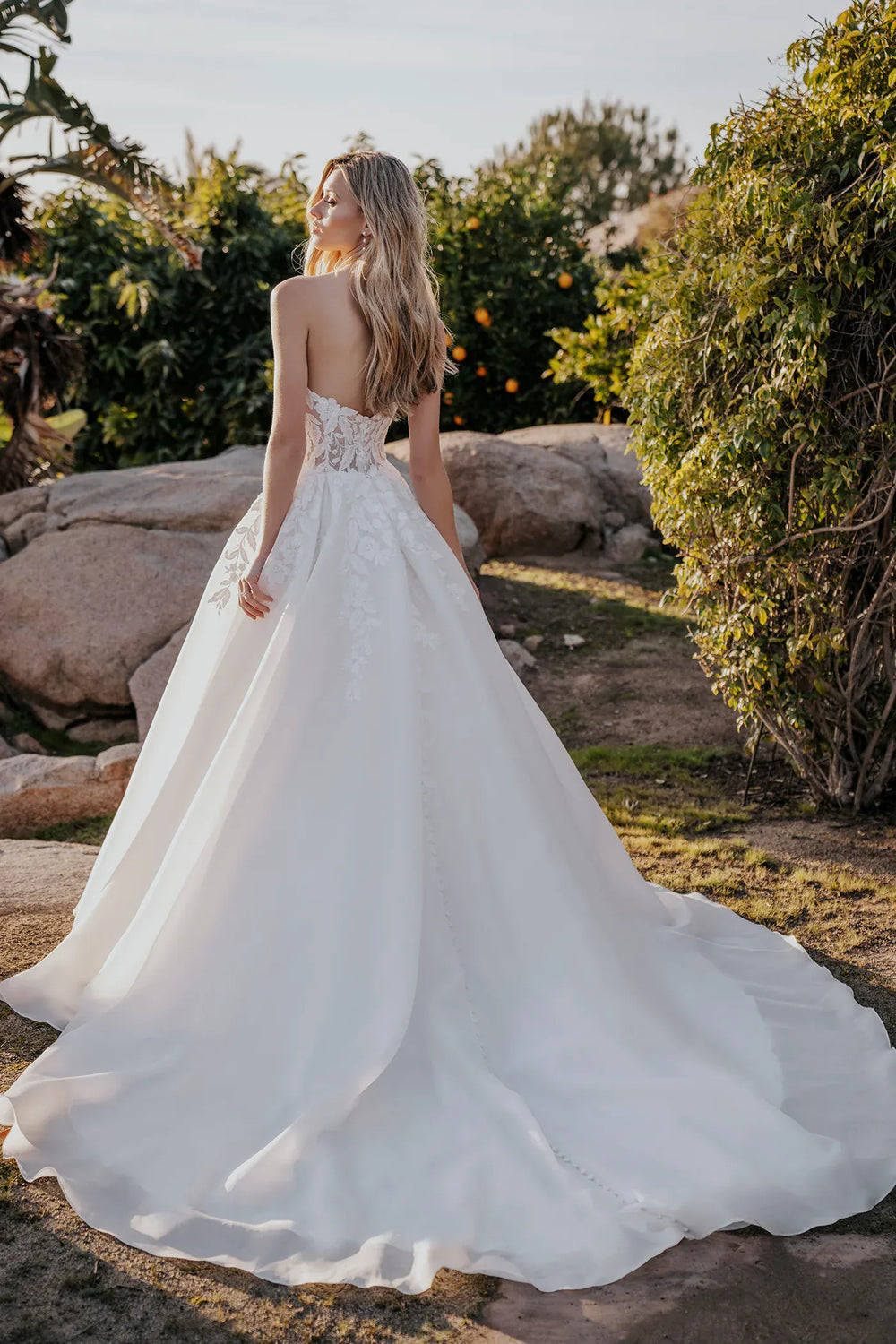 Woman in a white wedding dress standing outdoors with greenery in the background