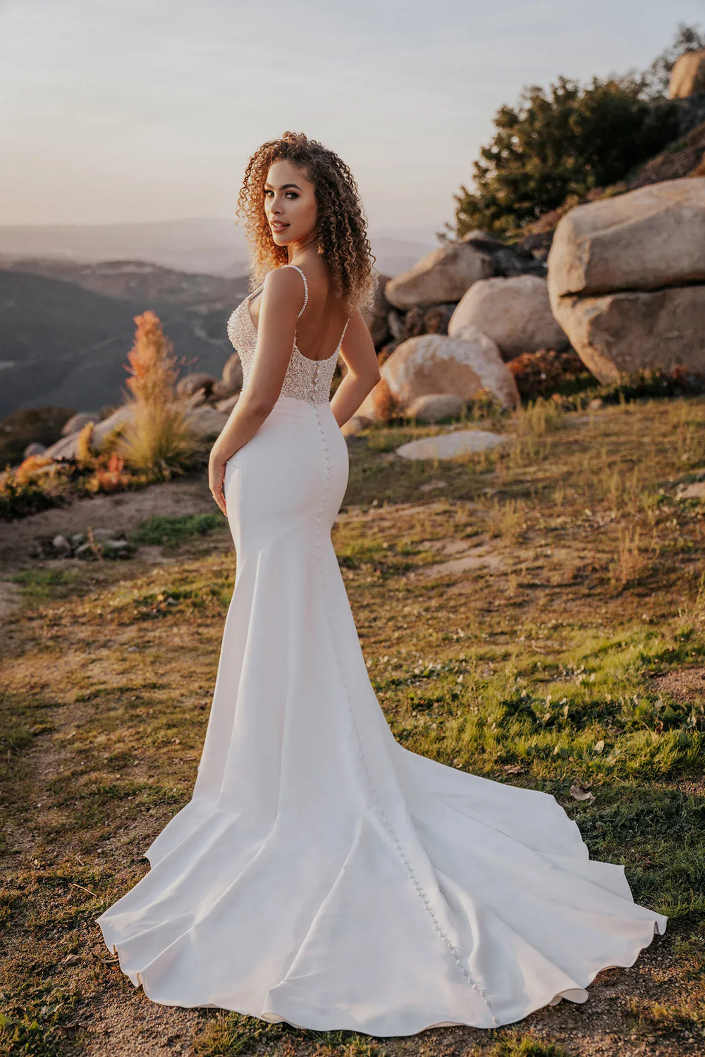 Woman in a white wedding dress standing in a natural landscape with mountains and rocks.