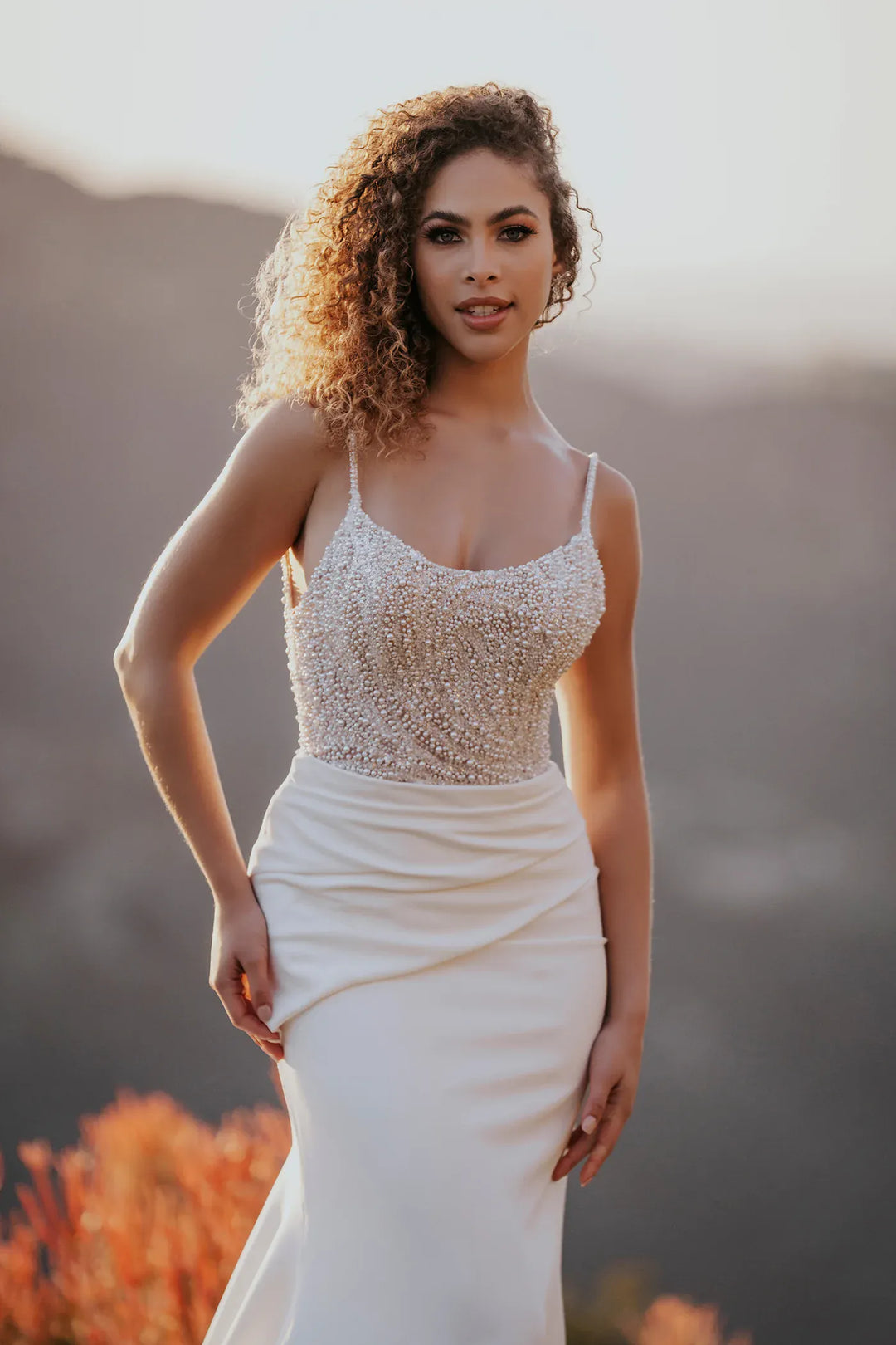 Woman in a white dress with a beaded top standing outdoors with mountains in the background