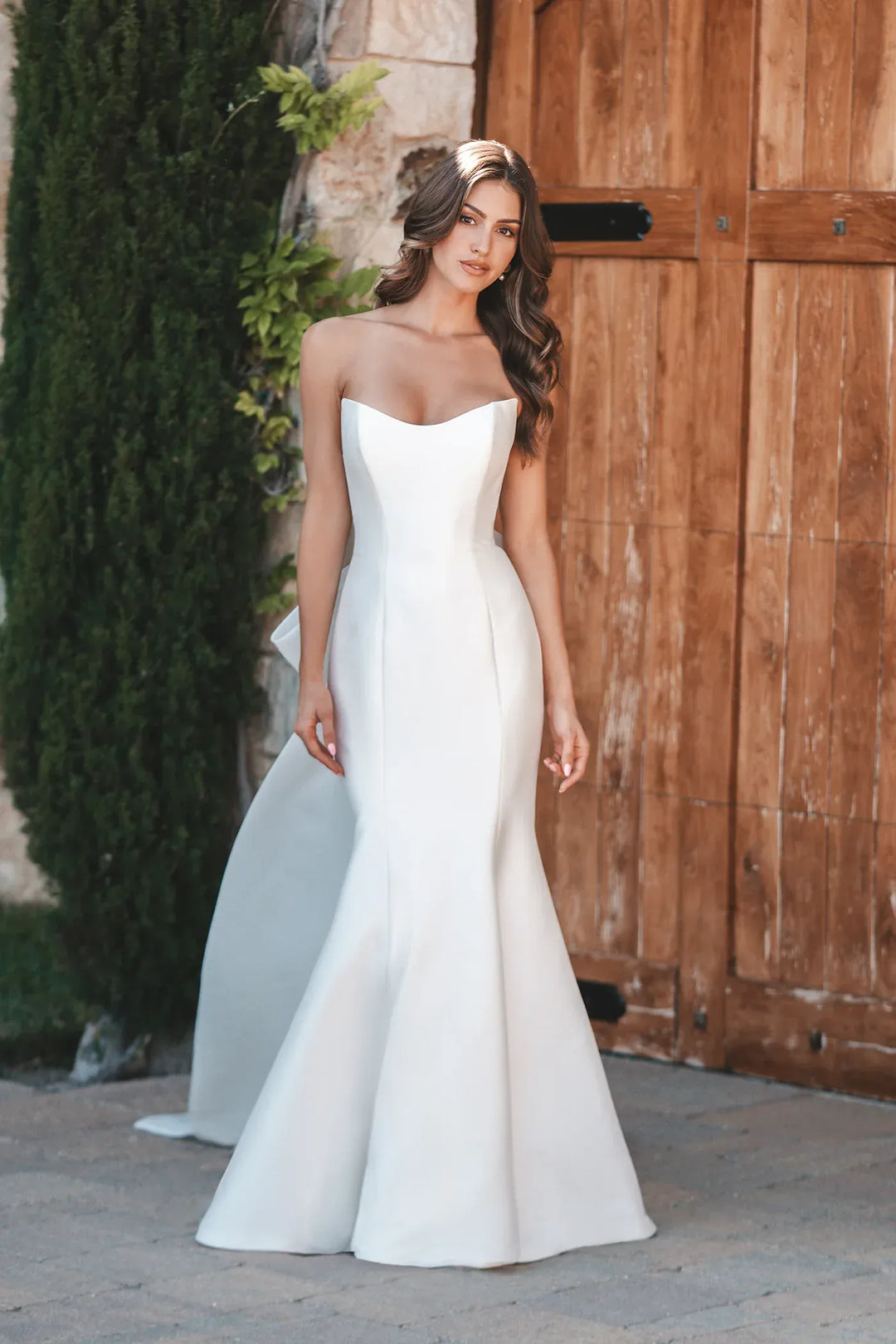 Woman in a white strapless gown standing in front of a wooden door.