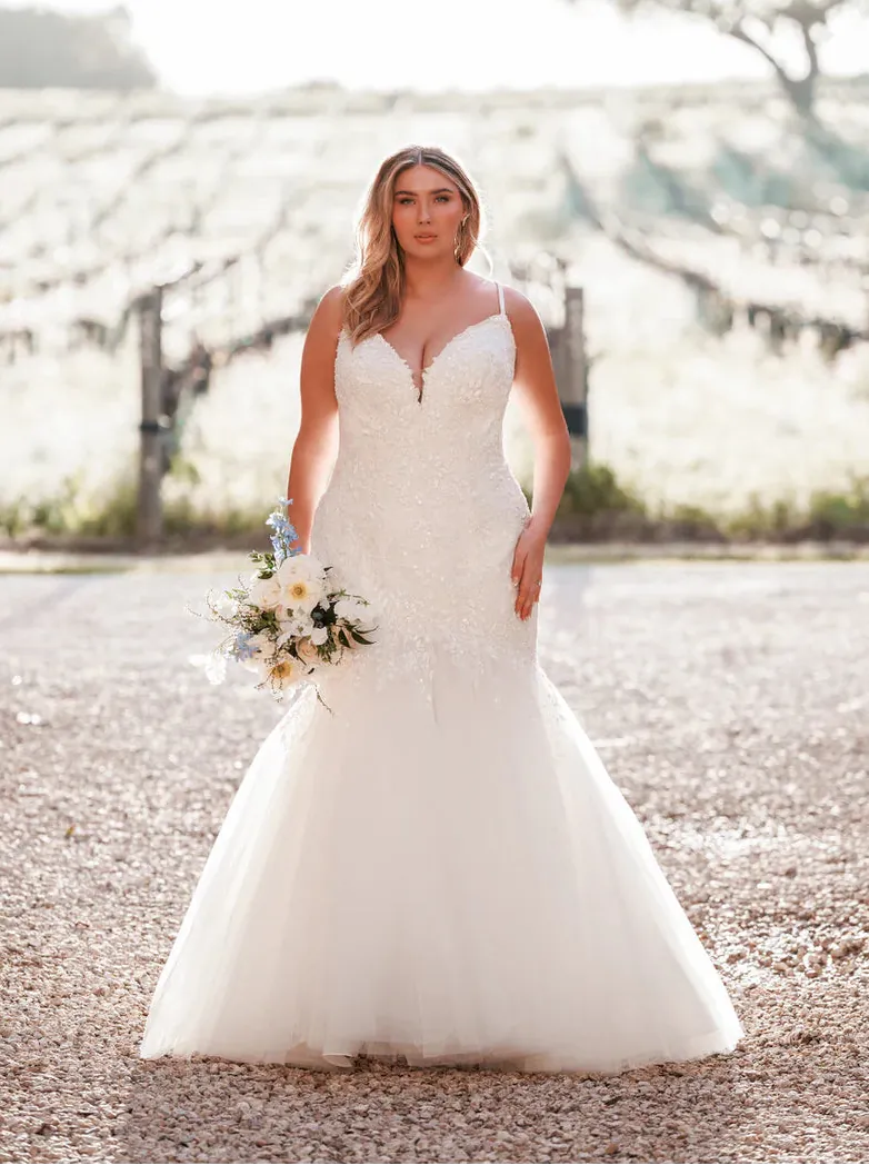 Woman in a white wedding dress holding flowers outdoors.