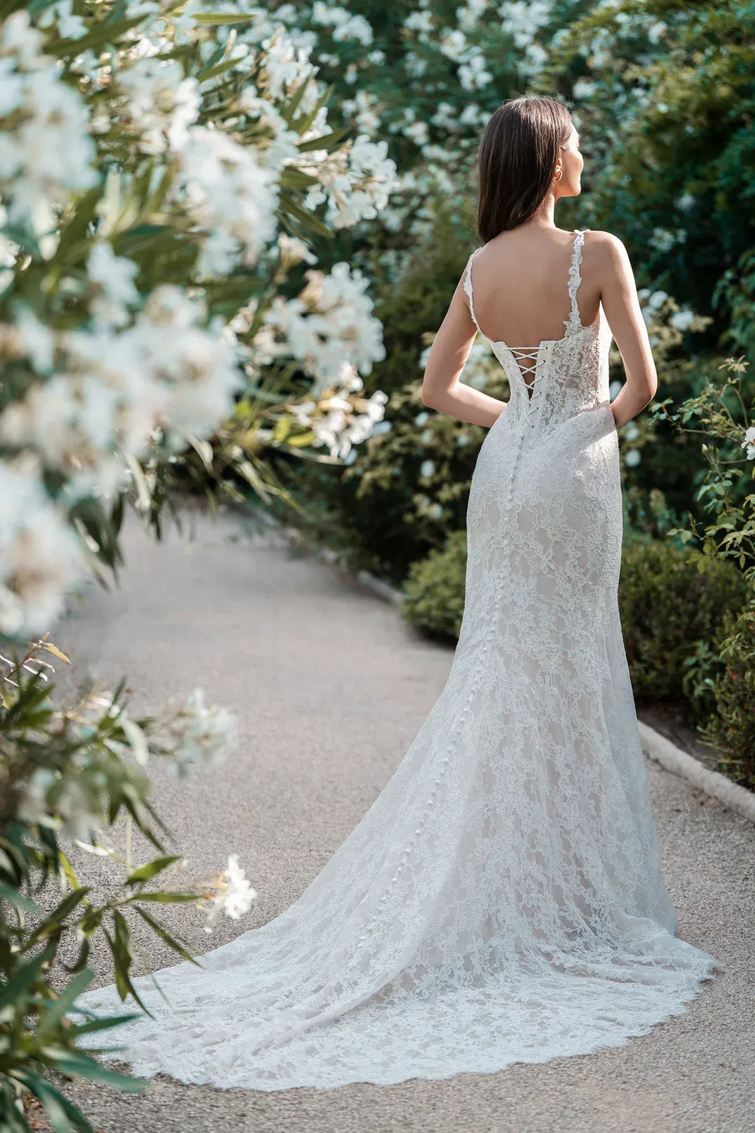 Woman in a lace wedding dress standing in a garden with white flowers.