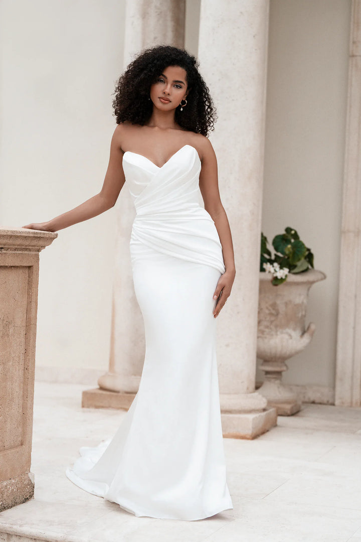 Woman in a white strapless gown standing in an elegant outdoor setting with columns and plants.