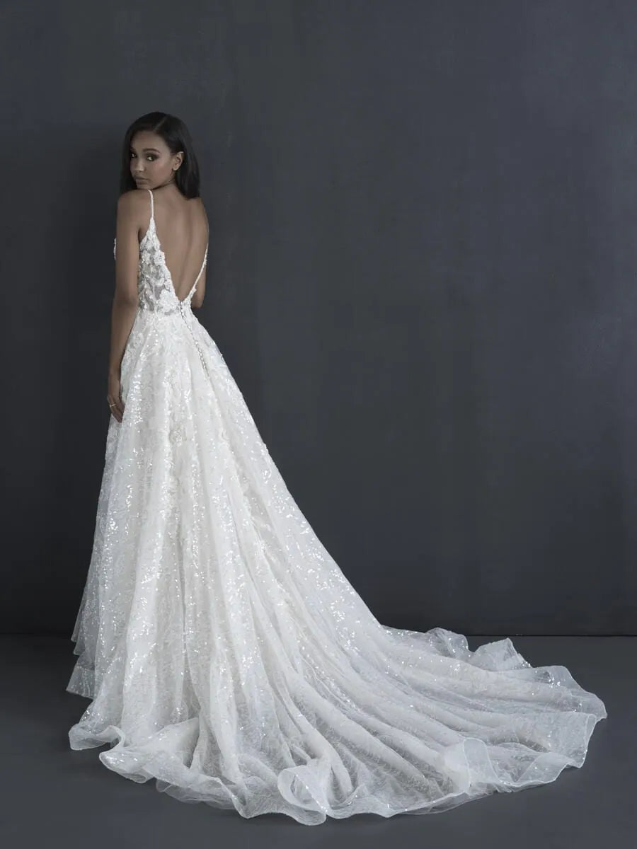 A model wearing a white lace wedding gown with a deep V-back and long train, photographed against a dark gray studio backdrop.
