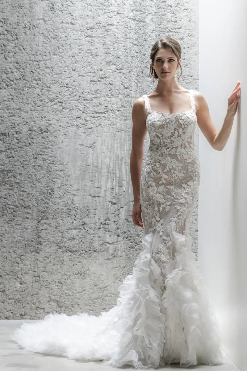 Woman wearing a white lace wedding dress against a textured wall.