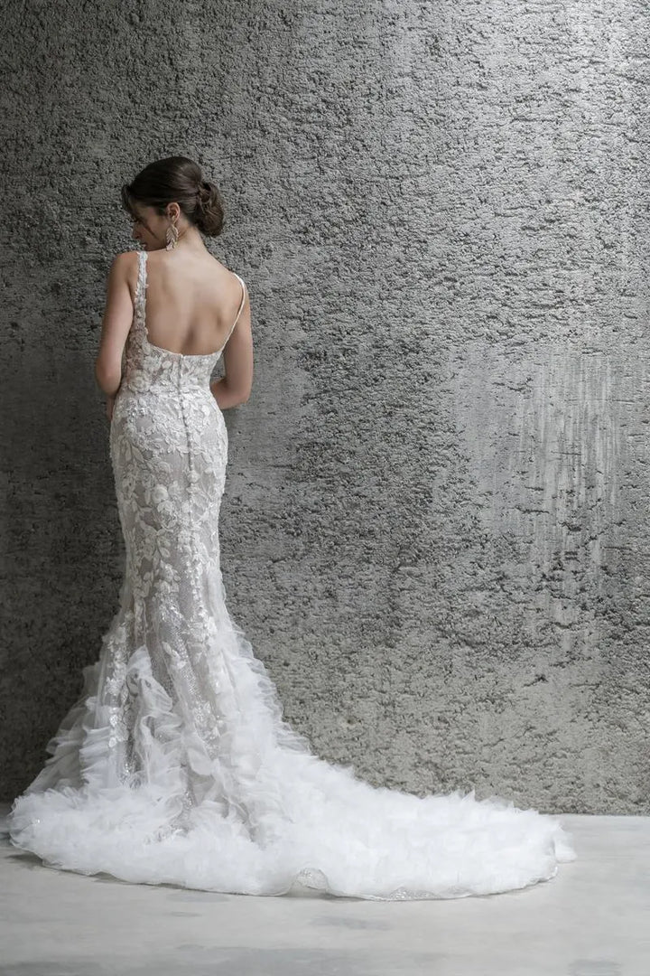 Woman in a white wedding dress with a long train against a textured gray wall.