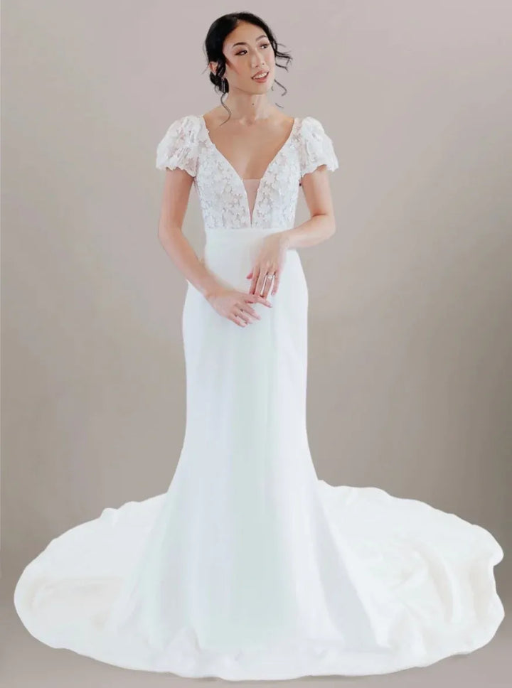 Woman wearing a white wedding dress with lace details on a plain background