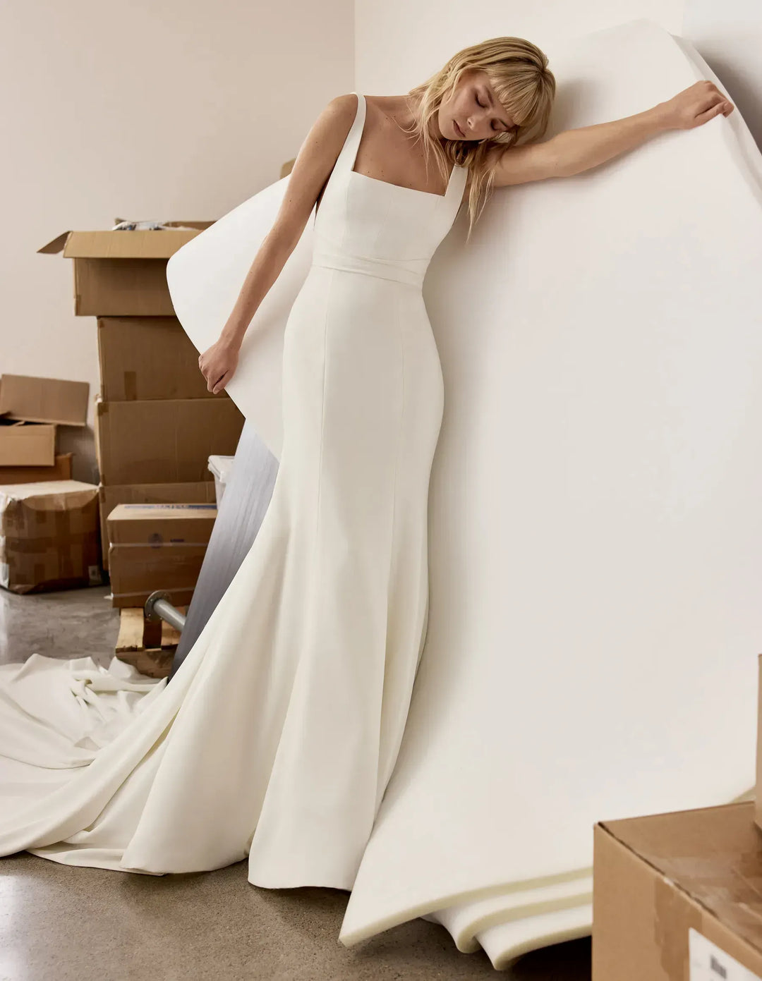 Woman in a white wedding dress standing among cardboard boxes.