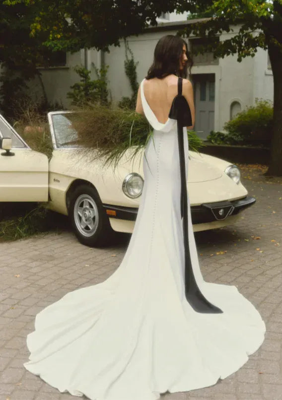back of alyne lillian ivory crepe fitted wedding dress with an open cowl and and black bow that drapes from the shoulder to the train