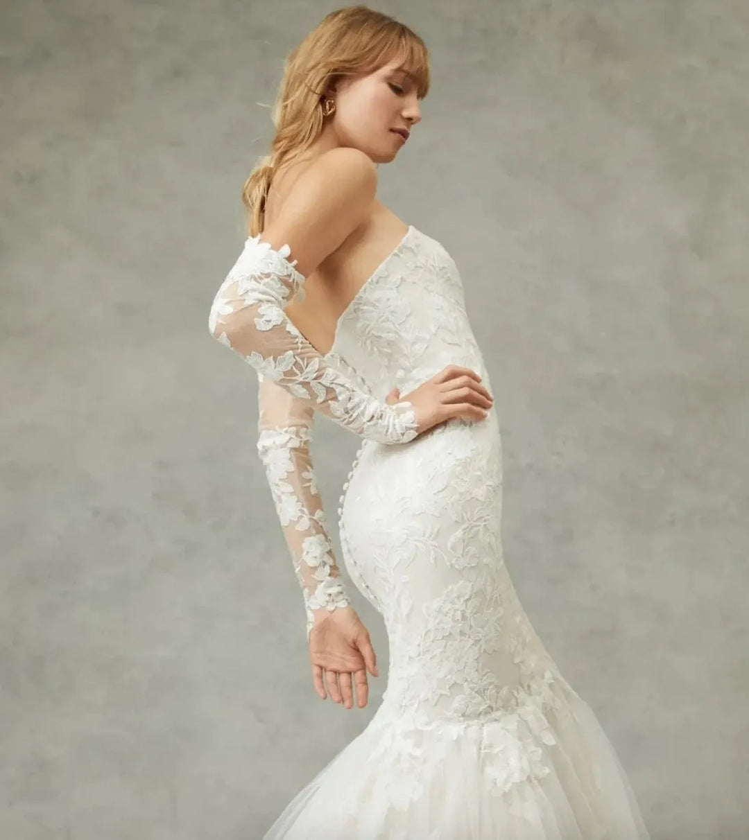 Woman wearing a white lace wedding dress with long sleeves against a neutral background