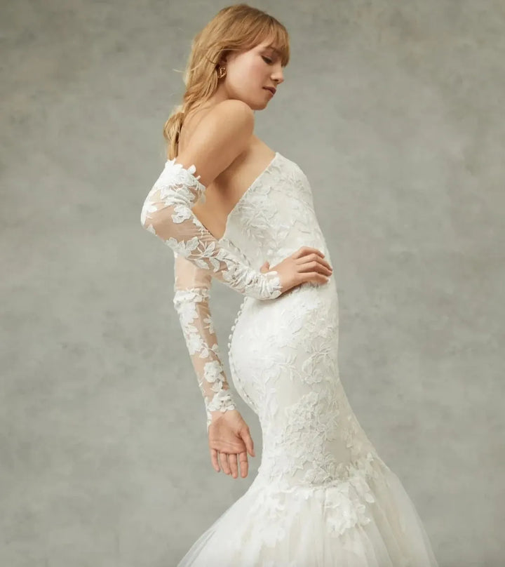Woman wearing a white lace wedding dress with long sleeves against a neutral background