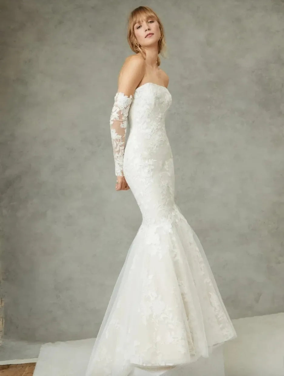 Woman wearing a strapless white wedding dress with long sleeves against a gray background