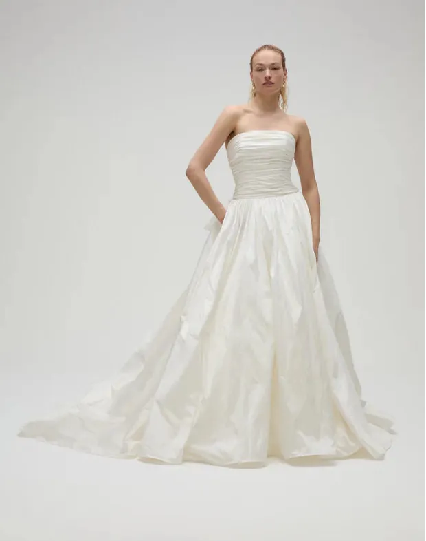 Woman wearing a strapless white wedding dress on a plain background