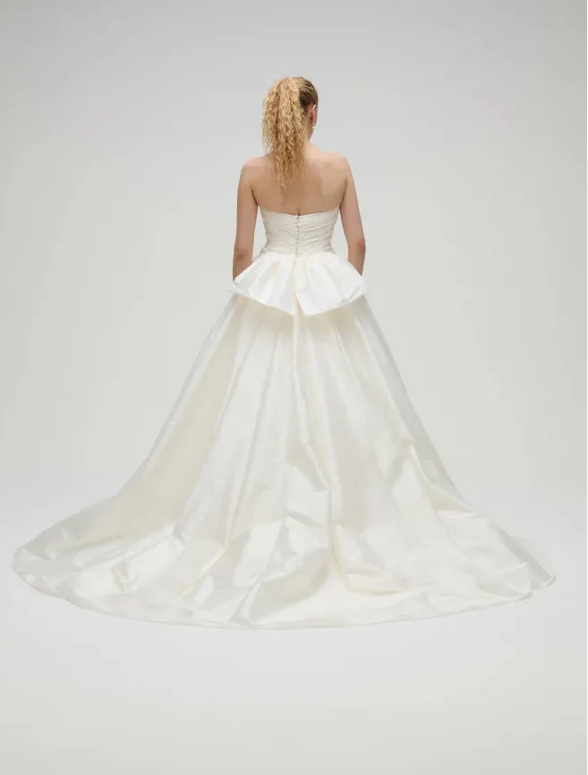 Woman wearing a white strapless gown with a flowing skirt on a plain background