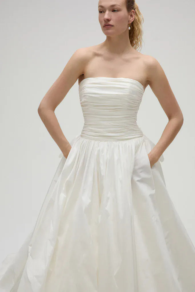 Woman wearing a strapless white wedding dress against a plain background