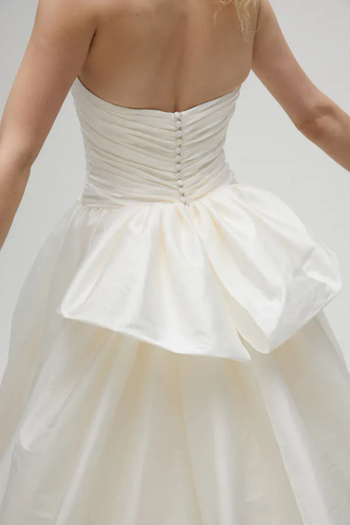 White strapless dress with a ruched bodice and flowing skirt on a plain background