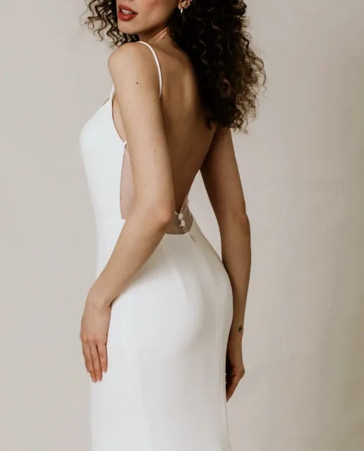 A woman wearing a white sleeveless backless dress, shown from the back and side against a plain light beige studio background.
