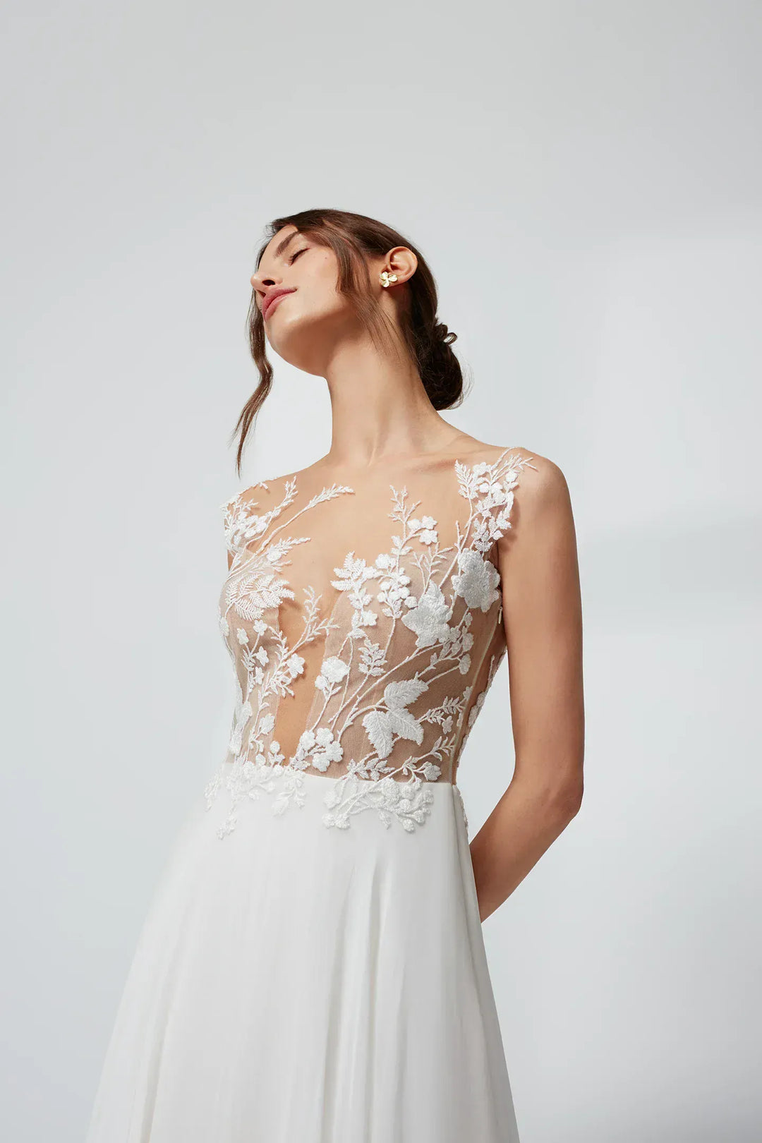Woman wearing a white wedding dress with floral lace details on a light gray background