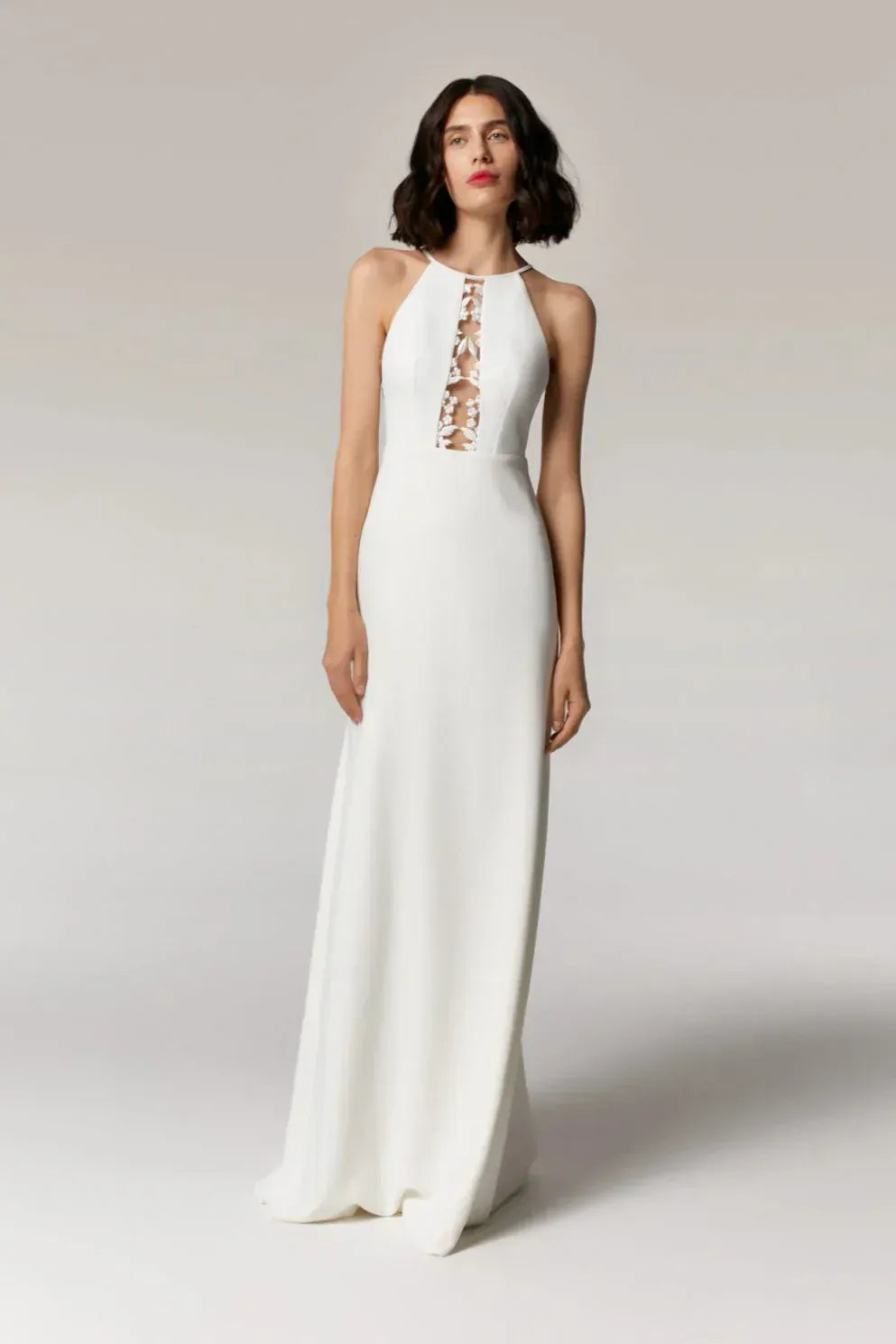 Woman wearing a white dress with floral embellishments on a plain background