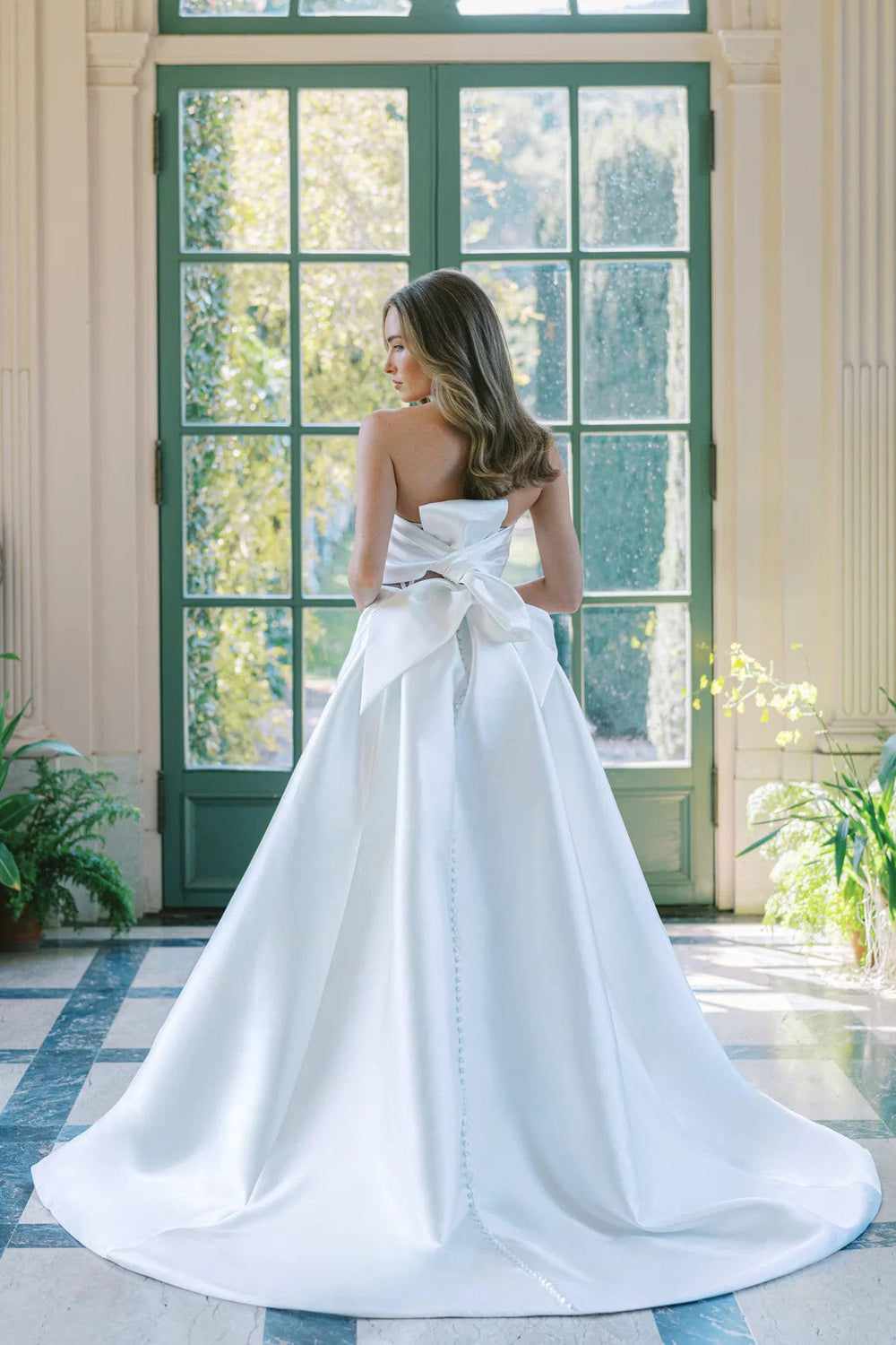 Woman in a white wedding dress standing in a room with large windows.