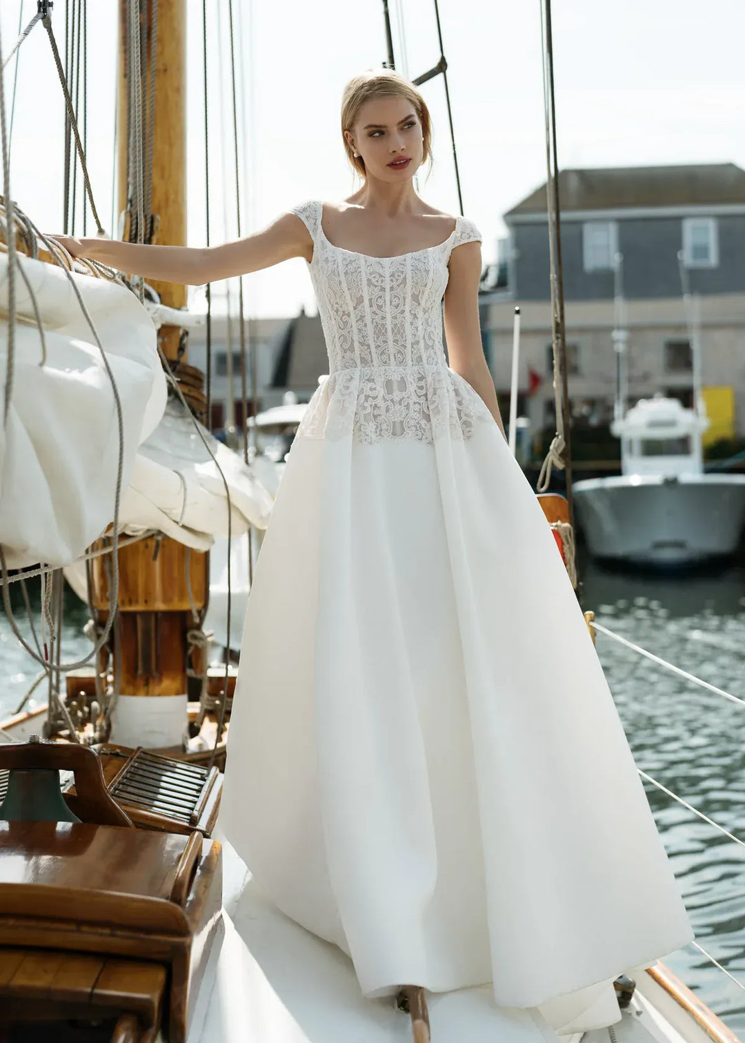 Woman in a white lace dress standing on a boat with water and buildings in the background