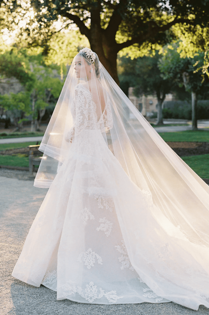 Bride in a white wedding dress with a long veil standing outdoors.