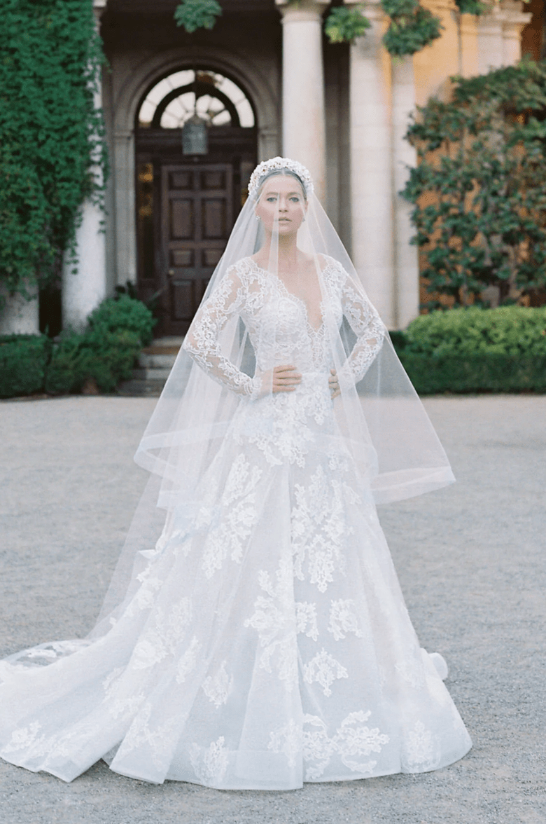 Woman in a white wedding dress with a long veil standing in front of a classical building.