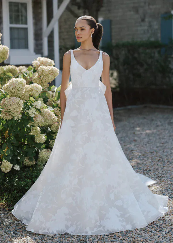 Woman in a white wedding dress standing outdoors with flowers and a building in the background