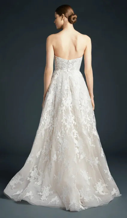 A strapless A-line wedding gown shown from the back on a model, featuring a fitted bodice, sheer lace overlay, and a full tulle skirt against a dark gray studio background.