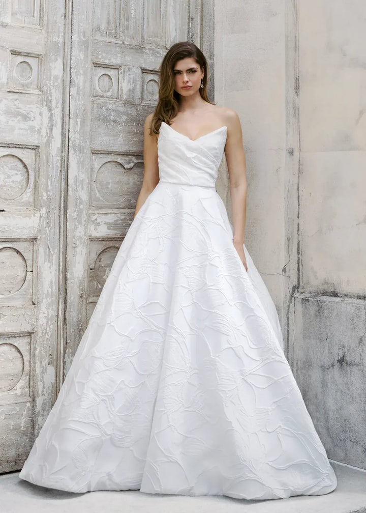Woman wearing a white wedding dress standing against a textured wall.