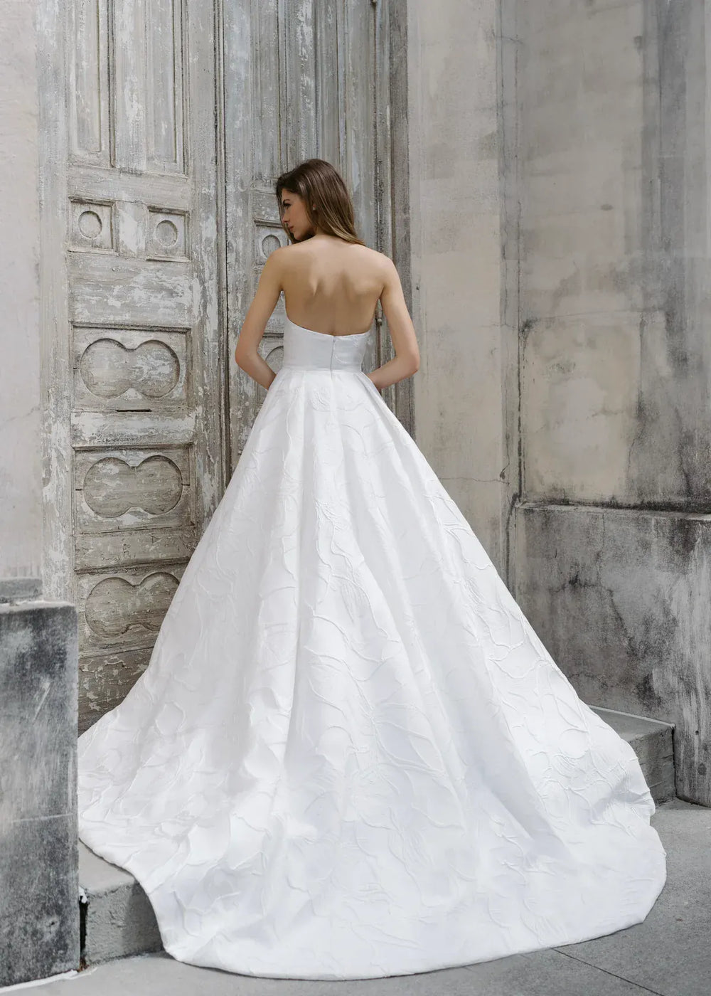 Woman in a white wedding dress standing against a textured stone wall.