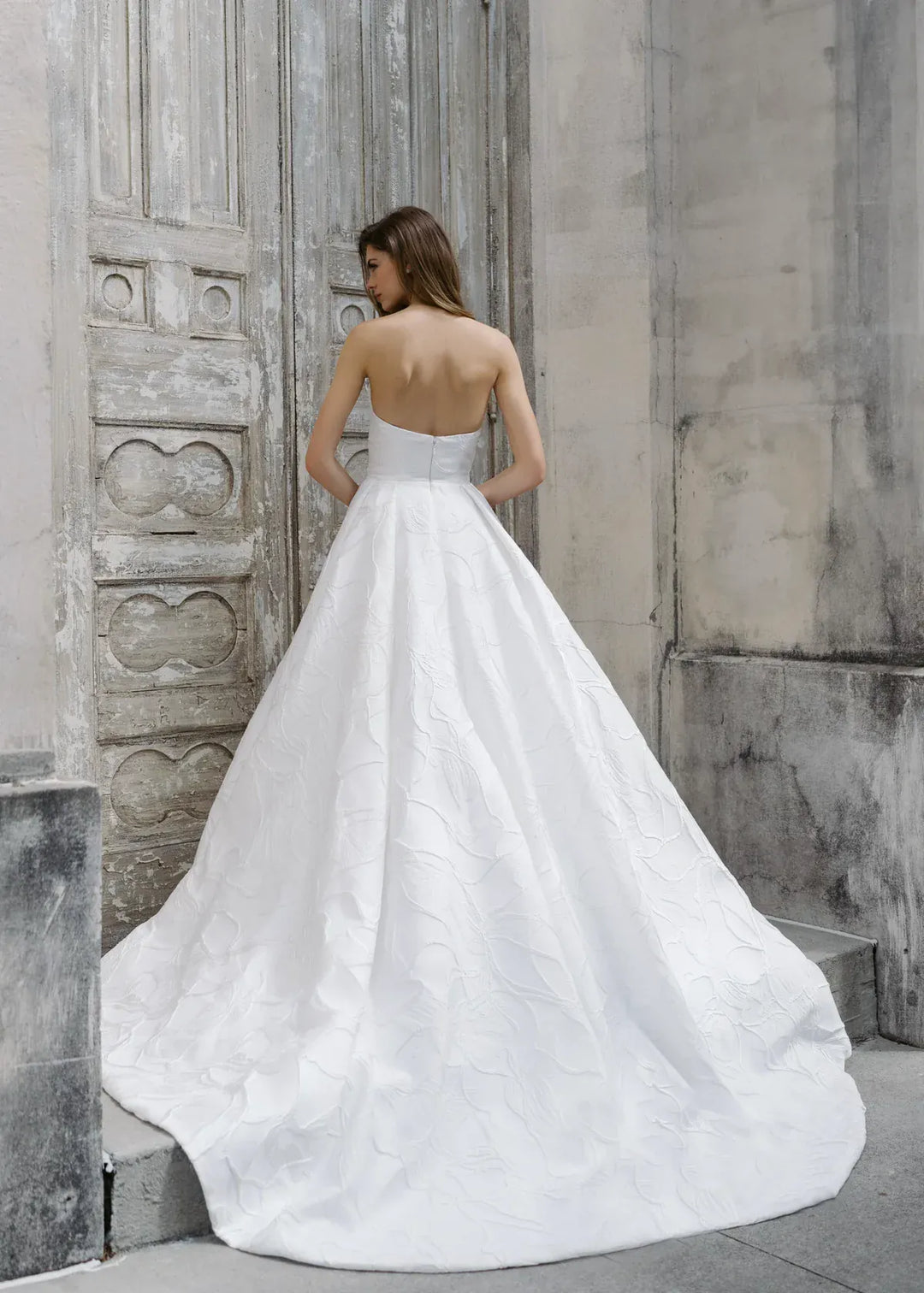 Woman in a white wedding dress standing against a textured stone wall.