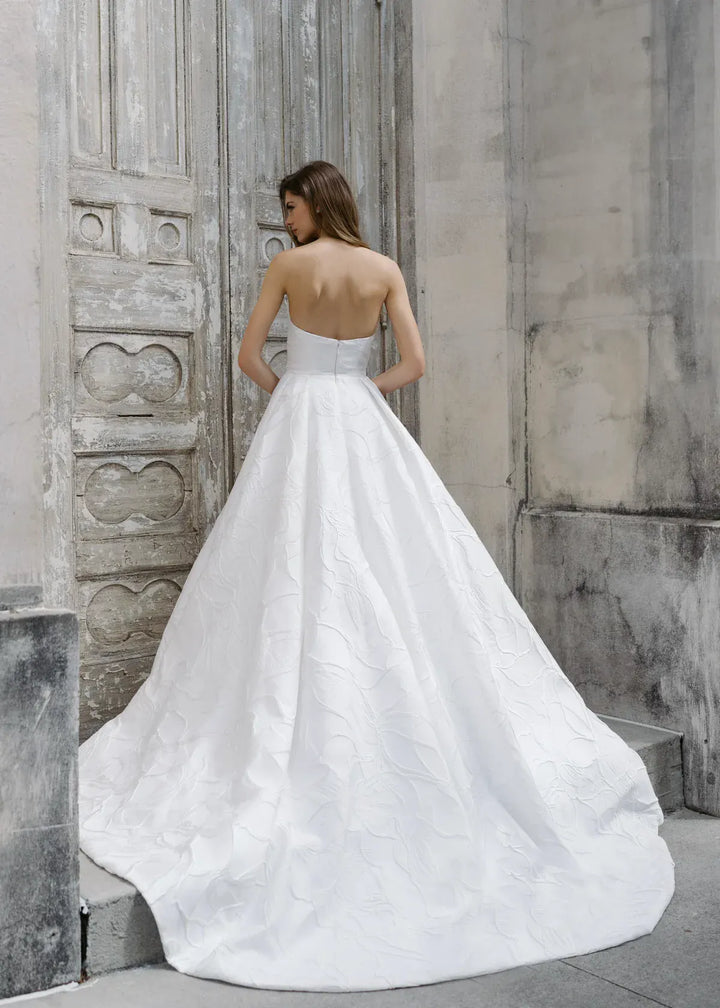 Woman in a white wedding dress standing against a textured stone wall.