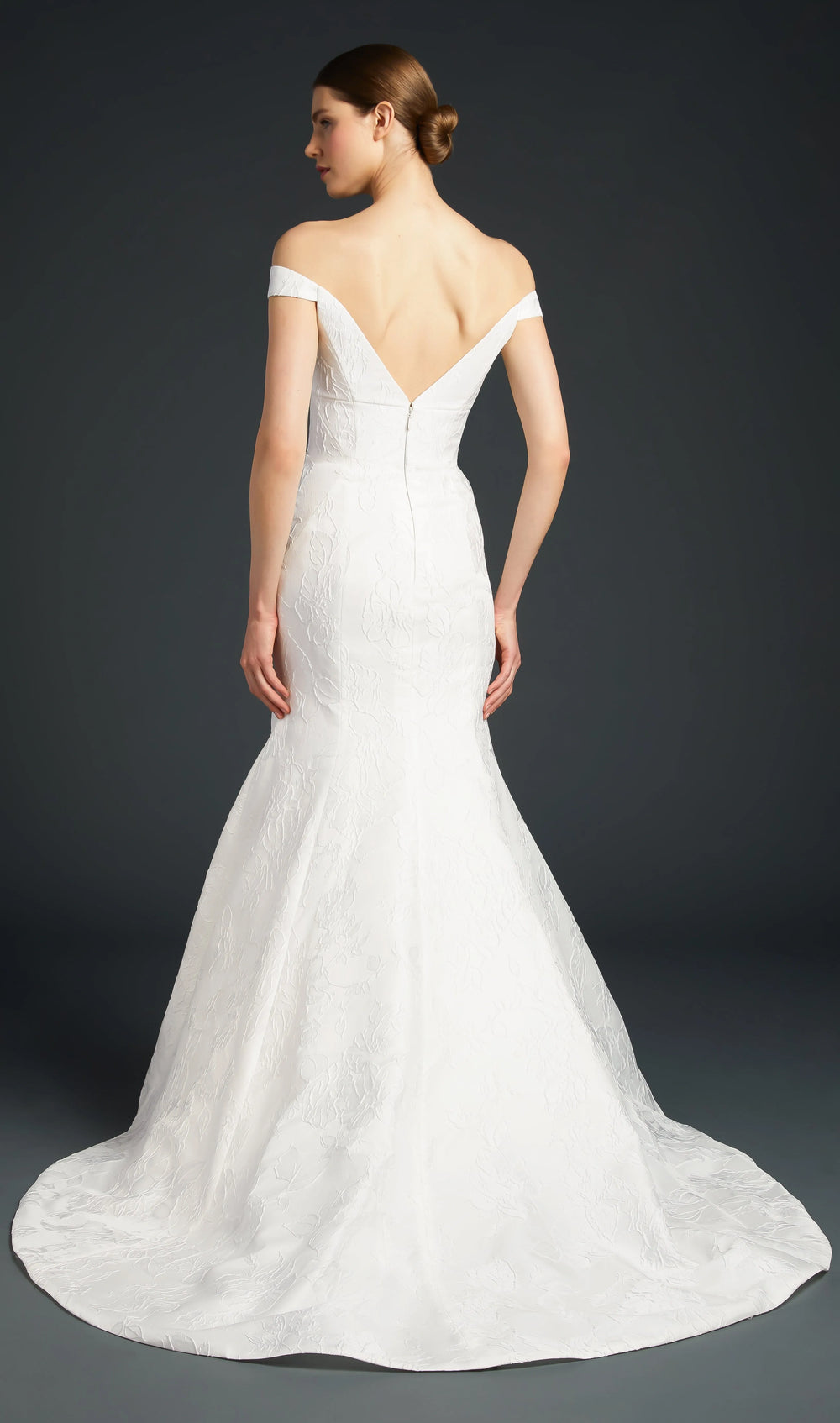 A white off-the-shoulder mermaid-style wedding gown shown from the back on a model against a dark gray studio background.