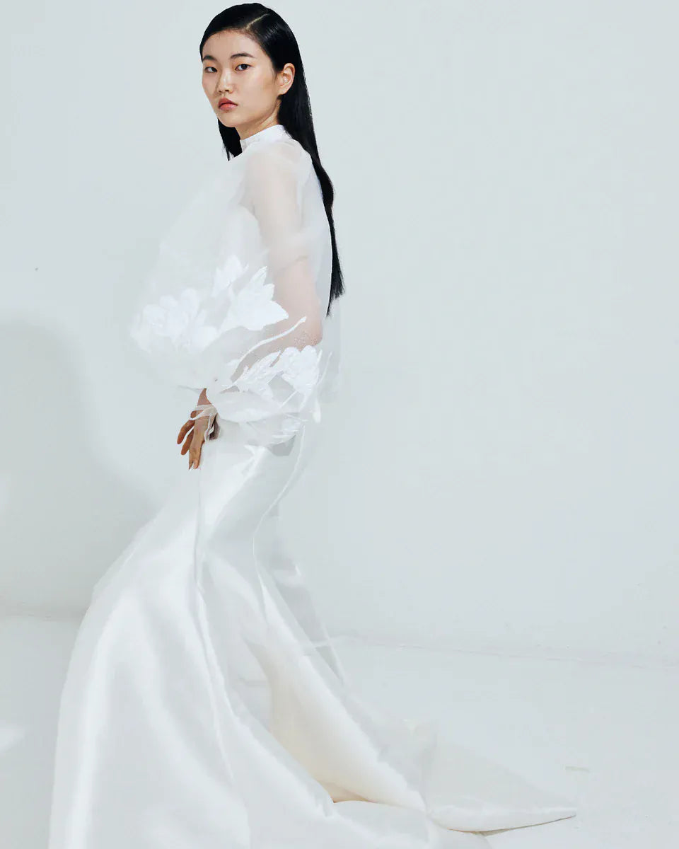 Woman wearing a white dress with floral details on a plain background