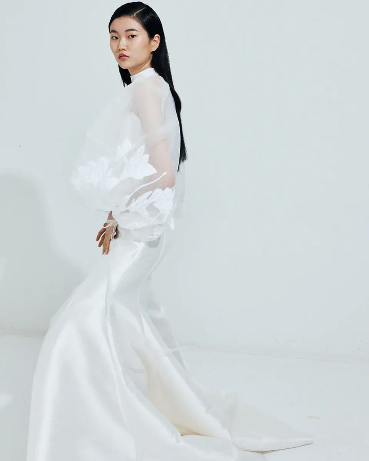 Woman wearing a white dress with floral details on a plain background