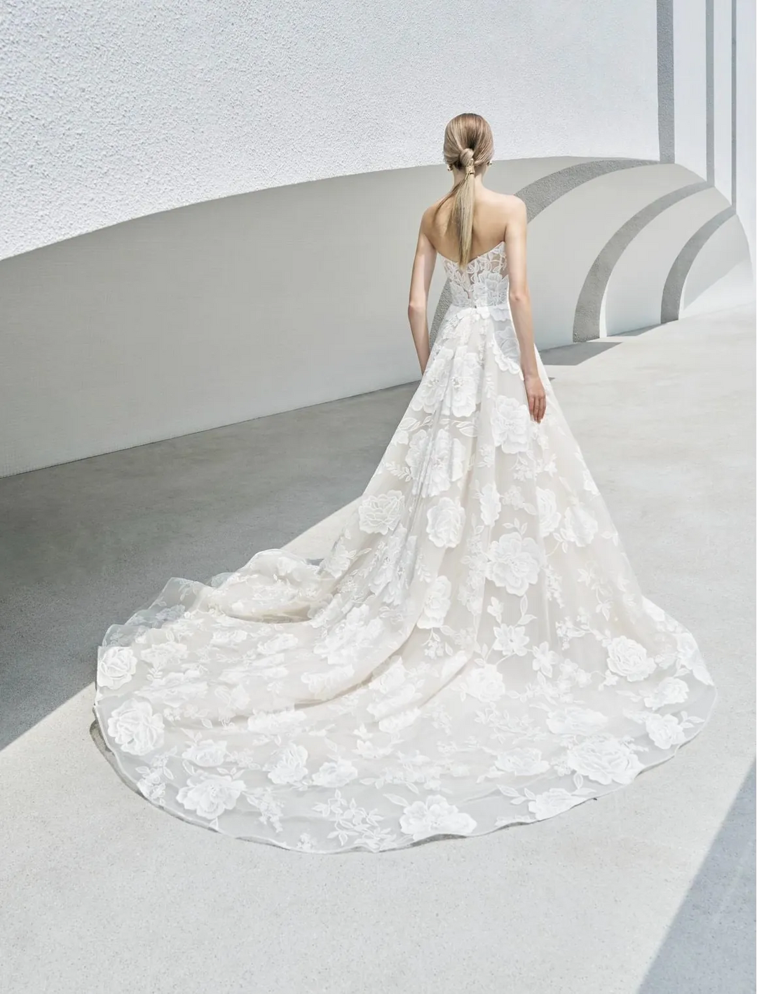 Woman in a white wedding dress with a long train standing in a minimalistic setting.