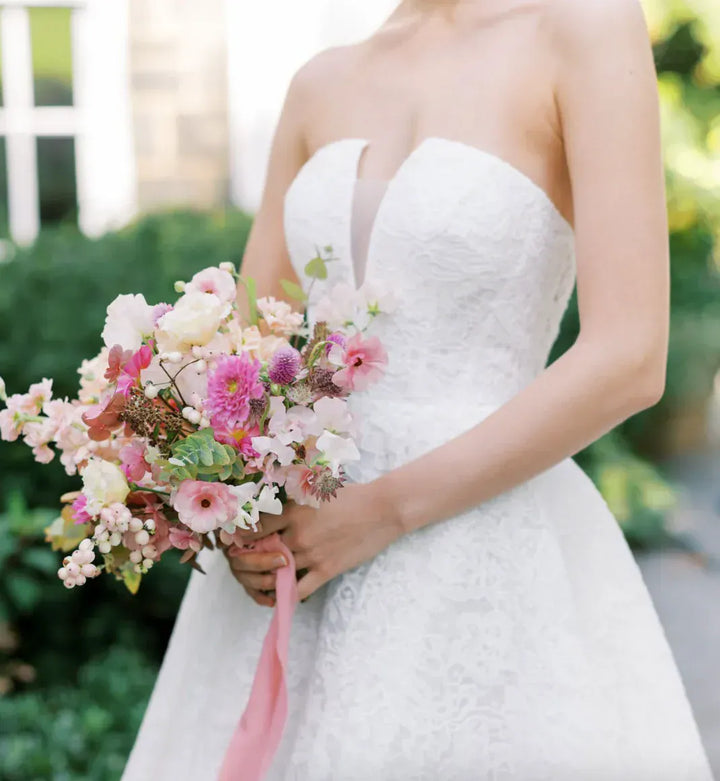 Bride in a strapless white wedding dress holding a bouquet of flowers with a blurred green background